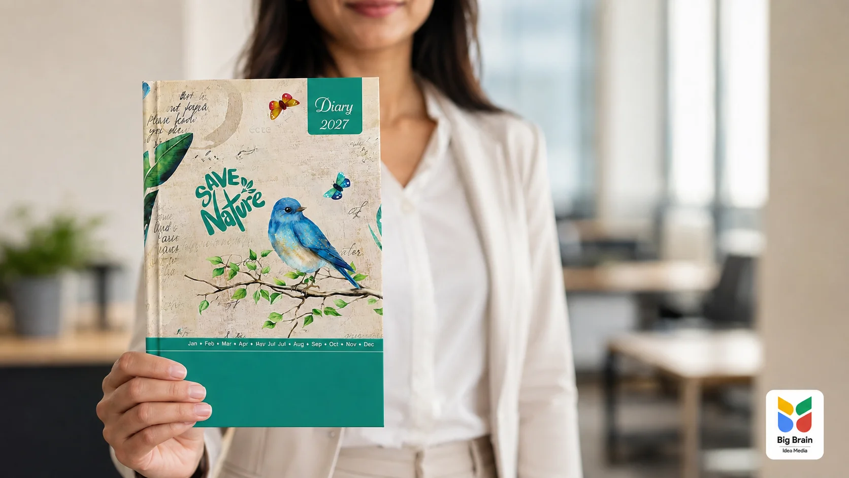A young professional woman holding a green 2027 customised corporate diary with a nature-themed cover in a modern office, featuring the Big Brain Idea Media logo.